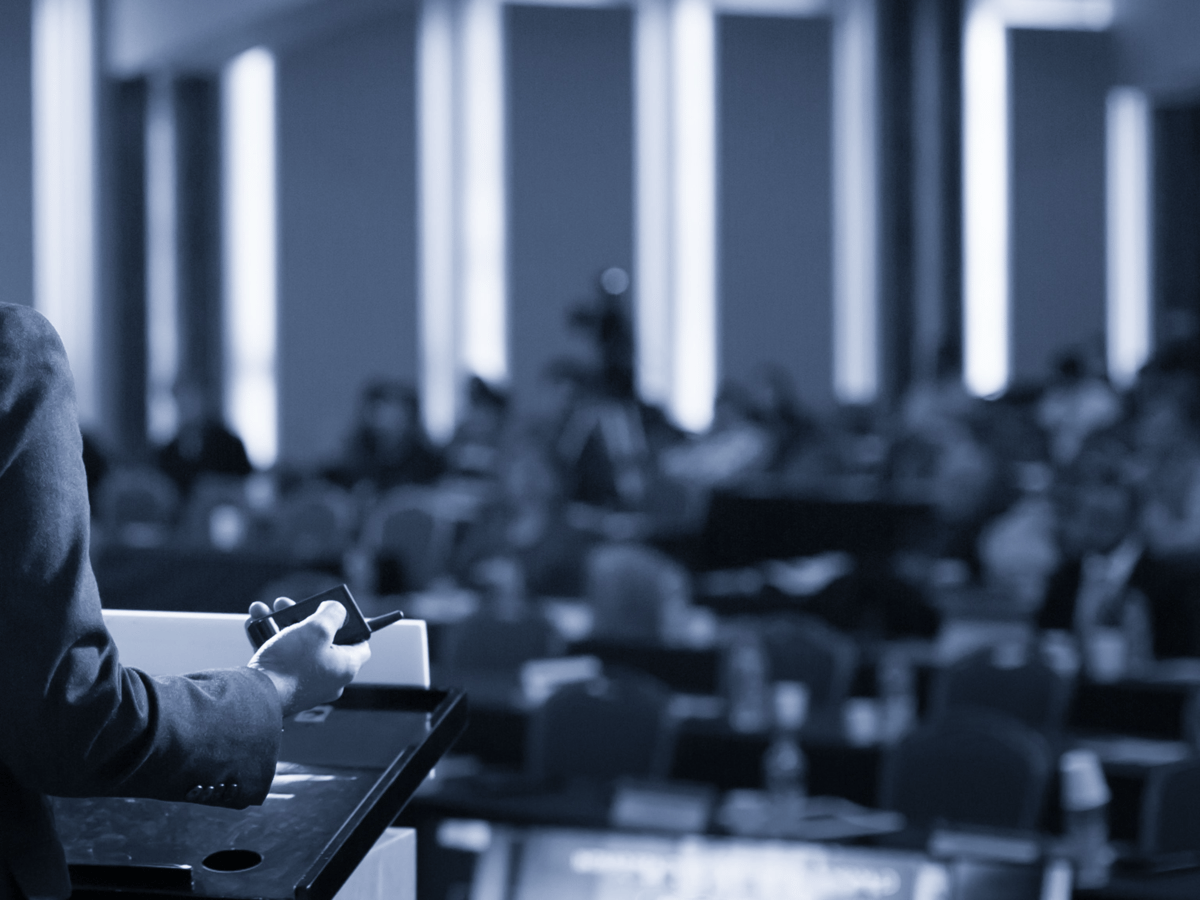 A speaker addressing an audience from a podium at a business conference