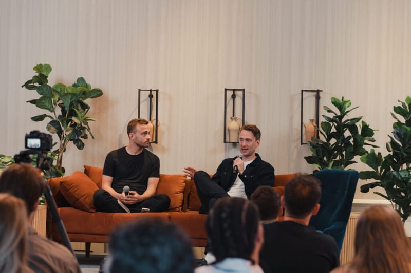 A fireside-chat session on stage with two speakers on an orange sofa in front of a seated audience