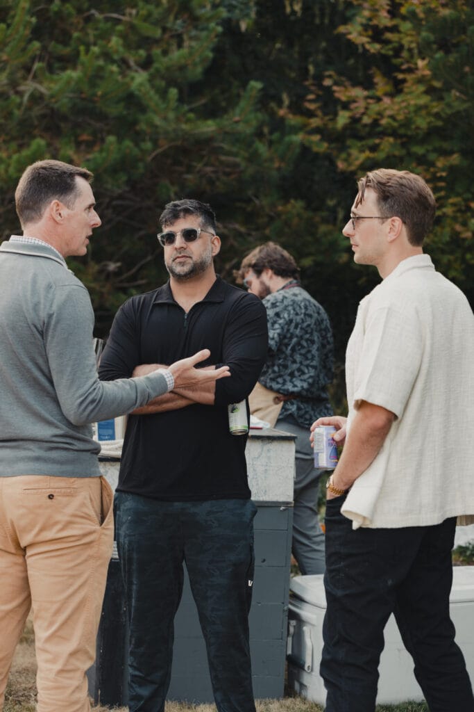 Three men talking outdoors at a casual evening gathering