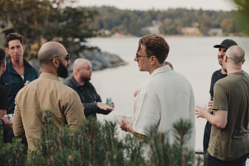 A group of men socializing with drinks by the waterfront at dusk